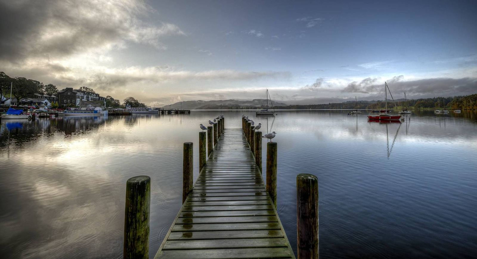 Windermere lake pier with moored sailing boats, gulls and fells beyond