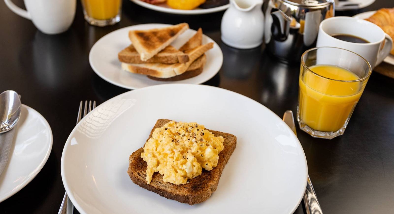 Scrambled eggs on toast with croissant, orange juice and coffee pot