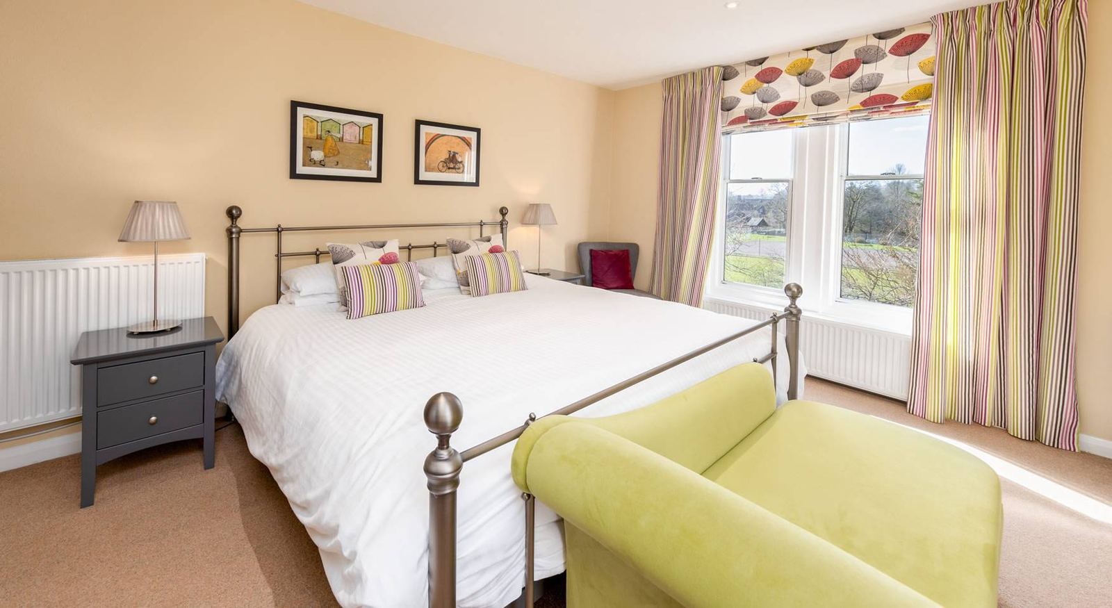 Classic Plus Superking bedroom with tall iron bed, parasol-print curtains, striped blinds and lime armchair