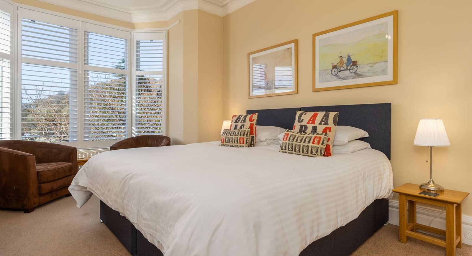 Classic Superking bedroom with navy headboard, bay shutters, cycling prints and letter-print cushions