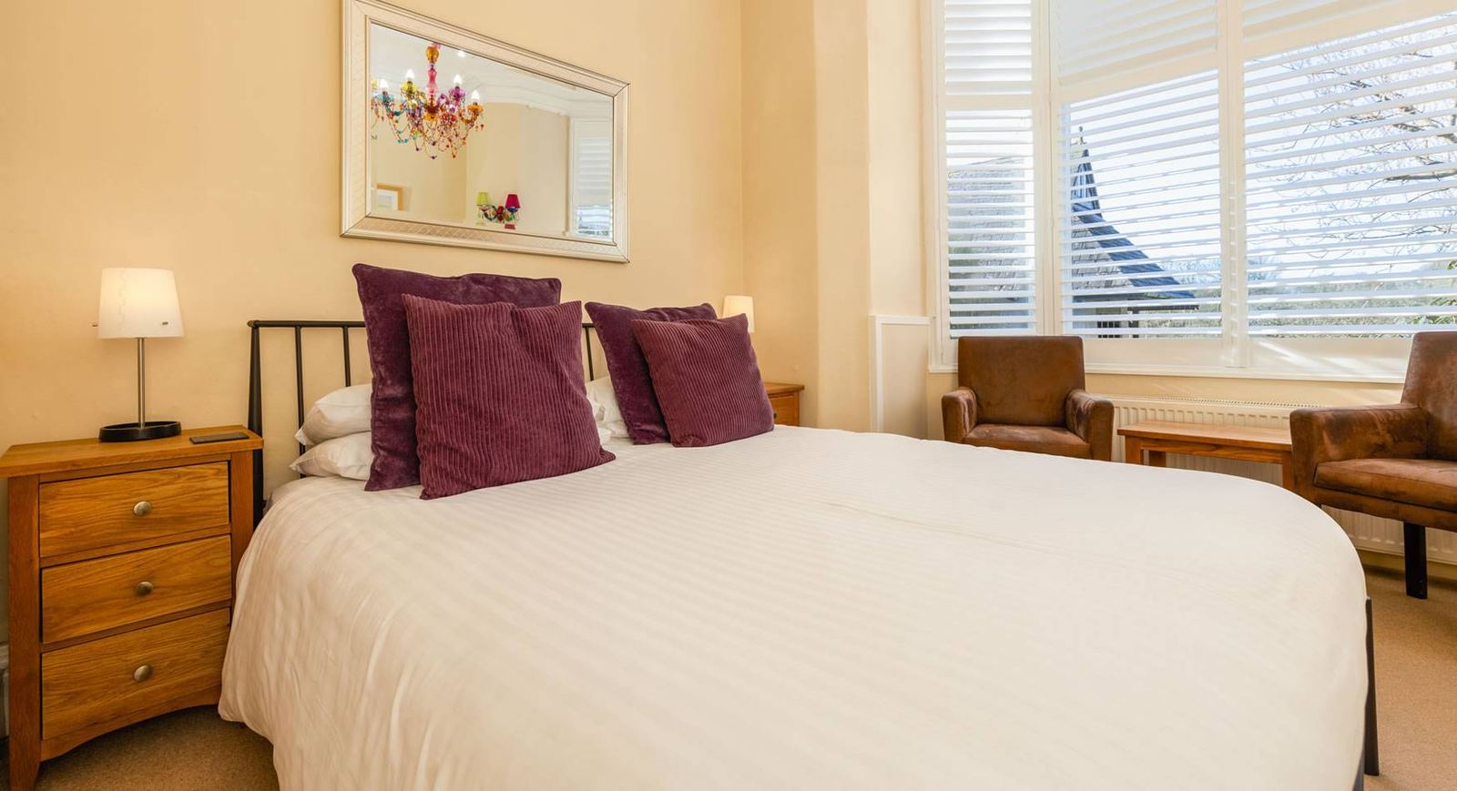 Classic bedroom with iron bedstead, deep-purple cushions and shutters, church spire visible through the window