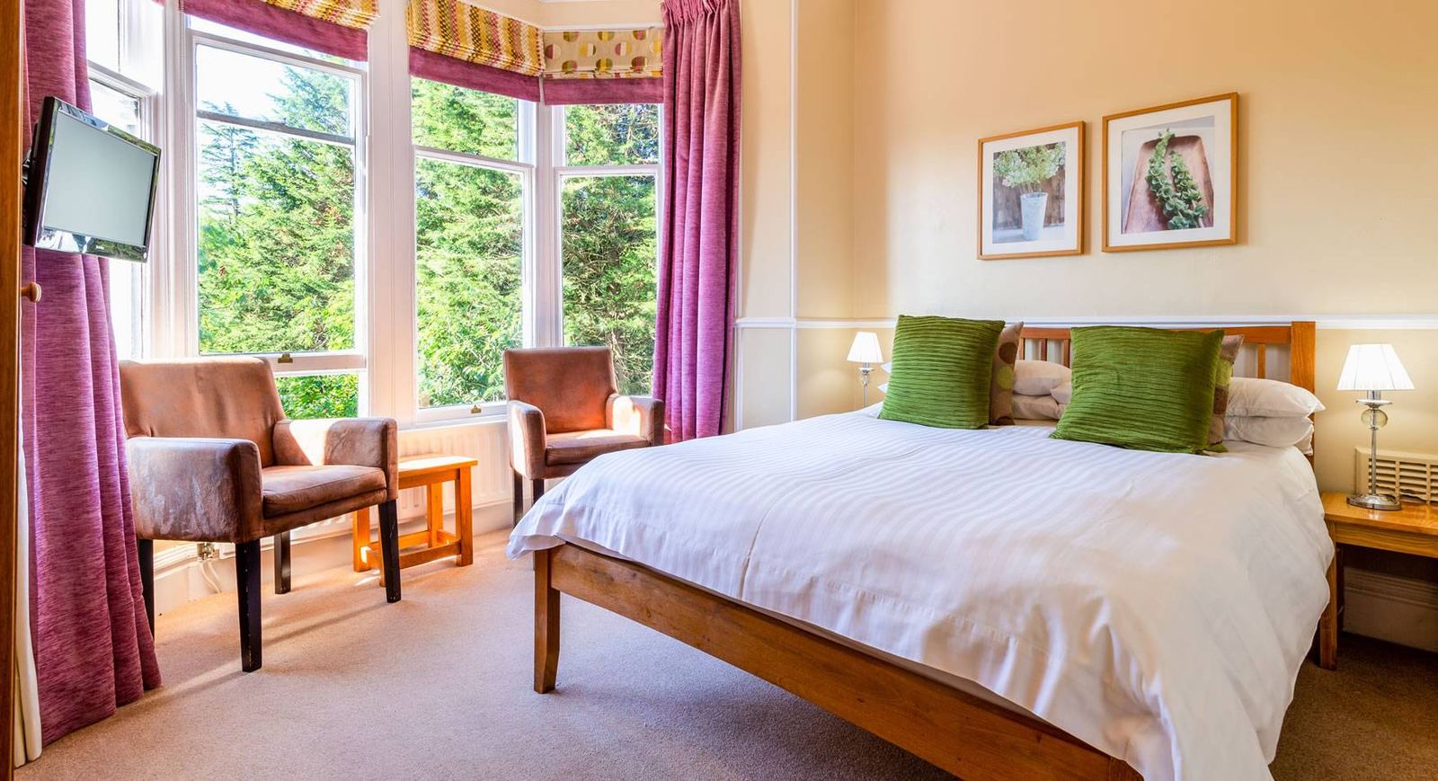 Cosy Double bedroom with bay window, magenta curtains, green cushions and two leather armchairs